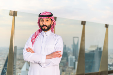 رجل أعمال سعودي باللباس السعودي التقليدي  ، يقف بشرفة عالية  وخلفه ابراج الرياض ، اطلاله رائعة لأبراج الرياض ، ناطحات السحاب في المملكة العربية السعودية 