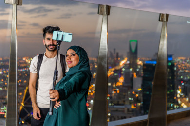 بنت سعودية مع شاب سعودي يلتقطان صورة سلفي بالهاتف المحمول , برج المملكة, أفق برج المملكة في اليوم الوطني, موسم الرياض, اليوم الوطني السعودي, أبراج الرياض
