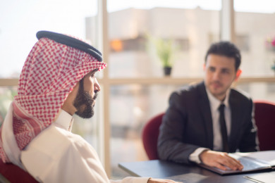 رجل اعمال سعودي عربي بلباس سعودي تقليدي  مع شريكه العربي بالبدلة , اجتماع عمل ، شركة سعودية ، بيئة عمل