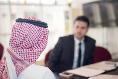 رجل اعمال سعودي عربي بلباس سعودي تقليدي  مع شريكه العربي بالبدلة , اجتماع عمل ، شركة سعودية ، بيئة عمل