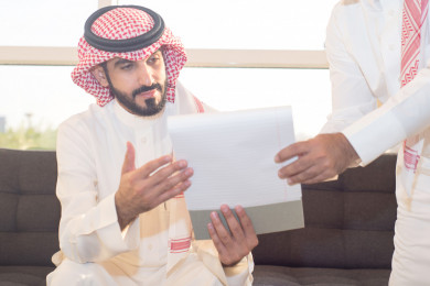 رجل اعمال سعودي يستلم عقد عمل من زميله . شركة سعودية ، زملاء عمل ، عقد شراكة ، بيئة عمل 
