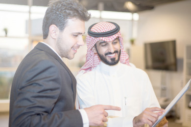 رجل اعمال سعودي عربي باللباس السعودي التقليدي ، يستلم عقد عمل من زميله بزي البدلة . شركة سعودية ، زملاء عمل ، عقد شراكة ، بيئة عمل 