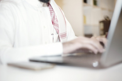 صورة مقربة لرجل اعمال سعودي خليجي على مكتب و يعمل على الكمبيوتر المحمول ، لباس السعودي التقليدي  ، شركة سعودية ، عمل الخليج ، وظيفة مكتبية ، بيئة عمل