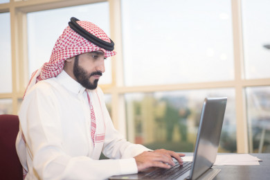 رجل اعمال سعودي خليجي على مكتب و يعمل على الكمبيوتر المحمول ، لباس السعودي التقليدي  ، شركة سعودية ، عمل الخليج ، وظيفة مكتبية ، بيئة عمل