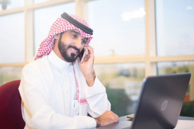 رجل اعمال سعودي خليجي على مكتب ، يتحدث بالهاتف المحمول ، لباس السعودي التقليدي  ، شركة سعودية ، عمل الخليج ، وظيفة مكتبية ، بيئة عمل