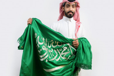 رجل  سعودي يمسك علم السعودية في يوم الوطني السعودي 