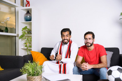 صديقان سعوديان يشاهدان مباراه للدوري السعودي ، كلاهما يشجعان فريق ألميريا ، ايماءات وجه مختلفة ، يجلسان على اريكة في غرفة المعيشة