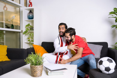 صديقان سعوديان يشاهدان مباراه للدوري السعودي ، كلاهما يشجعان فريق ألميريا ، ايماءات وجه مختلفة ، يجلسان على اريكة في غرفة المعيشة