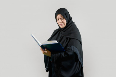 امرأة سعودية تقرأ كتاب، كبيرة بالسن ترتدي عباءة, بخلفية بيضاء