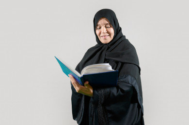 امرأة سعودية تقرأ كتاب، كبيرة بالسن ترتدي عباءة, بخلفية بيضاء