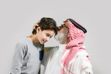 جد سعود يقبل رأس حفيده, كبير بالسن خليجي يرتدي ثوب و شماغ بخلفية بيضاء