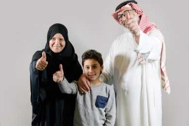 بورتريه عائلة سعودية يشاورون بالإبهام، مكونة من جد و جدة كبار بالسن و طفل, بخلفية بيضاء