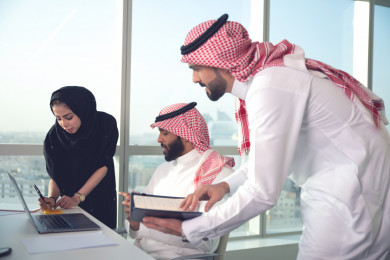 فريق عمل سعودي خليجي باجتماع اونلاين مع العميل باستخدام الكمبيوتر المحمول ، تسجيل ملاحظات على دفتر الملاحظات ، شركاء عمل