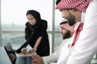 فريق عمل سعودي خليجي باجتماع اونلاين مع العميل باستخدام الكمبيوتر المحمول ، تسجيل ملاحظات على دفتر الملاحظات ، شركاء عمل