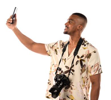 بورتريه لشاب عربي خليجي سعودي يقوم بالتقاط صور سيلفي من خلال الهاتف المحمول، مصور يحمل كاميرا عالية الدقة، شاب اسمر، بشرة سمراء، ارتداء ملابس كاجوال، خلفية بيضاء
