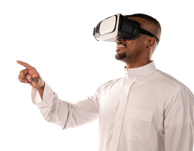بورتريه لشاب أسمر عربي خليجي سعودي يرتدي نظارة الواقع الإفتراضي ثلاثية الأبعاد، يشير بأصبع السبابة لشئ ما يشاهده بالواقع الإفتراضي، إستخدام حاسة اللمس، محاكاة العالم الافتراضي، خلفية بيضاء