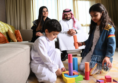 عائلة سعودية جميلة مجتمعة  في غرفة المعيشة والأطفال يلعبان على الأرض 