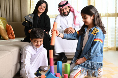 عائلة سعودية جميلة مجتمعة  في غرفة المعيشة والأطفال يلعبان على الأرض 