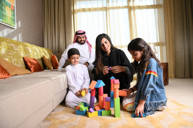 عائلة سعودية جميلة مجتمعين في غرفة المعيشة والأطفال يلعبنا على الأرض 