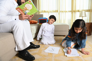 عائلة سعودية في غرفة المعيشة والأولاد يرسمون على الورقة في ارض المجلس 