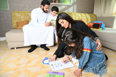 عائلة سعودية في غرفة المعيشة والأولاد يرسمون على الورقة في ارض المجلس 