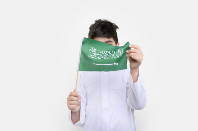 بورتريه فتى عربي سعودي يمسك علم السعودية بيده ، اليوم الوطني السعودي، احتفالات السعودية، بخلفية بيضاء