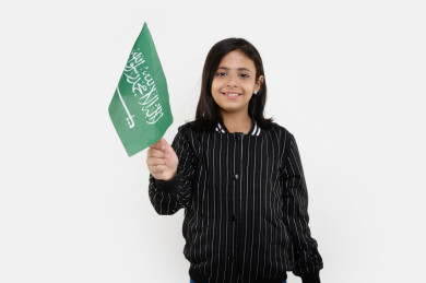 بورتريه فتاه عربية سعودية تمسك علم السعودية بيدها ، ترفرف بيدها علم السعودية ، على خلفية بيضاء