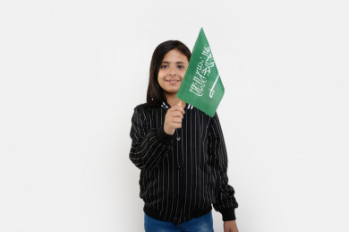 بورتريه فتاه عربية سعودية تمسك علم السعودية بيدها ، ترفرف بيدها علم السعودية ، على خلفية بيضاء