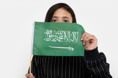 بورتريه فتاه عربية سعودية تمسك علم السعودية بيدها . على خلفية بيضاء