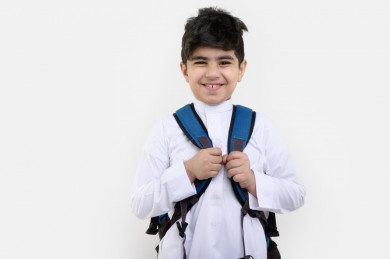 بورتريه لفتى طالب مدرسي سعودي مبتسم ينظر الى الكاميرا ، يرتدي حقيبة ظهر مدرسية ، و يرتدي ثوب سعودي تقليدي ،مدرسة سعودية