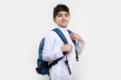 بورتريه لفتى طالب مدرسي سعودي مبتسم ينظر الى الكاميرا ، يرتدي حقيبة ظهر مدرسية ، و يرتدي ثوب سعودي تقليدي ،مدرسة سعودية