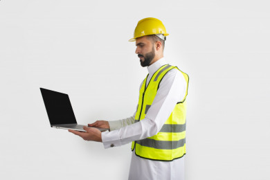 مهندس معماري عربي سعودي  ، استخدام الكمبيوتر المحمول ، رجل  انشاءات باللباس السعودي ، خوذة المهندس ،خلفية بيضاء