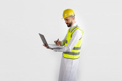مهندس معماري عربي سعودي يسجل بيانات المشورع ، استخدام الكمبيوتر المحمول ، رجل  انشاءات باللباس السعودي ، خوذة المهندس ،خلفية بيضاء