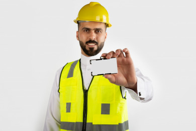 مهندس معماري سعودي مبتسم بيده بطاقة تعريفيه بيضاء  ، خوذة عمل صفراء ، خلفية بيضاء 