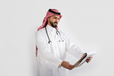 بورتريه رجل طبيب عربي سعودي يتابع ملف تشخيص لحالة المريض ، طبيب خليجي باللباس السعودي ، ملف التشخيص ، خلفية بيضاء