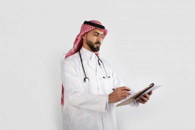بورتريه رجل طبيب عربي سعودي  يسجل بيانات على ملف تشخيص المريض ، طبيب خليجي باللباس السعودي ، ملف التشخيص  ، خلفية بيضاء