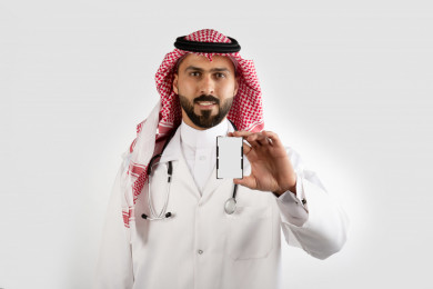 بورتريه رجل طبيب سعودي عربي مسلم ، طبيب خليجي باللباس السعودي ، بيده بطاقة تعريفية بيضاء ، خلفية بيضاء