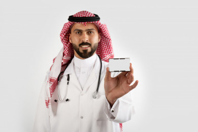 بورتريه رجل طبيب سعودي عربي مسلم ، طبيب خليجي باللباس السعودي ، بيده بطاقة تعريفية بيضاء ، خلفية بيضاء