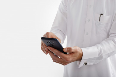 صورة مقربة لرجل سعودي خليجي ، لبس سعودي تقليدي ، استخدام الهاتف المحمول ، خلفية بيضاء