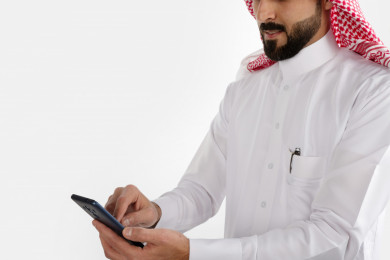 صورة مقربة لرجل سعودي خليجي ، لبس سعودي تقليدي ، استخدام الهاتف المحمول ، خلفية بيضاء