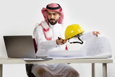 بورتريه مهندس معماري سعودي خليجي محترف  في مكتب العمل ، يتابع العمل على مخططات البناء ، يخطط لمشروع جديد , مهندس انشاءات خليجي بالثوب السعودي ، مخطط البناء ، خوذة العمل ، خلفية بيضاء 