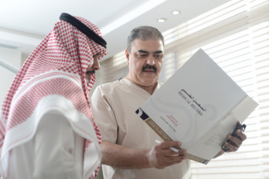 دكتور سعودي يتحدث مع مريض و يقدم اسشارات طبية في العيادة, طبيب خليجي يحمل تقرير طبي 