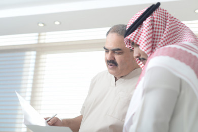دكتور سعودي يتحدث مع مريض و يقدم اسشارات طبية في العيادة, طبيب خليجي يحمل تقرير طبي 