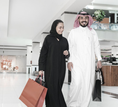 زوجان جميلان مع أكياس تسوق يتحدثان ويبتسمان أثناء القيام بالتسوق في المركز التجاري ,  زوجين سعوديين يستمتعان بالتسوق مع بعضهما 