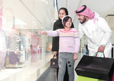 فتاة سعودية صغيرة تشير إلى شيء على واجهة المتجر , عائلة سعودية تنظر إلى واجهة المتجر في المول 
