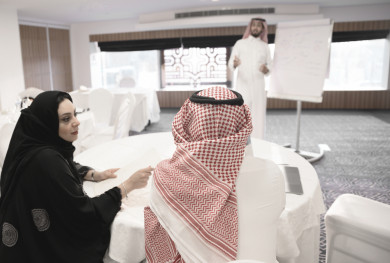 مدرب عربي سعودي يقوم بالشرح على سبورة بيضاء مع متدربان سعوديان يتحدثان  ، رجل اعمال سعودي يتحدث عن  استراتيجيات الشركة على لوحة بيضاء ، دورات تدريبية ، غرفة اجتماعات ، اجتماع عمل