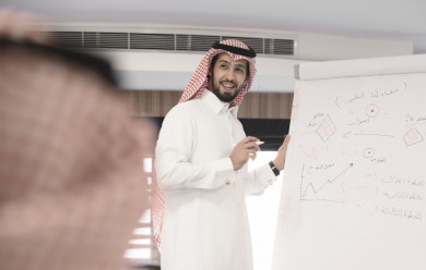 صورة مقربة لمدرب سعودي خليجي مبتسم يشرح على لوح ابيض  ، رجل اعمال في اجتماع لشرح استراتيجيات الشركة ، غرفة اجتماعات ، اجتماع عمل ، دورة تدريبية