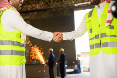مهندسان صناعيان سعوديين شركاء في مصنع الحديد ، يتصافحان لبدء مشروع جديد ، باللباس السعودي التقليدي ،شرارة لحام الحديد مبعثرة بالخلفية ، مفهوم الهندسة و الصناعة
