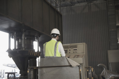 صورة مقربة لمهندس صناعي سعودي في مصنع الحديد ، يقوم بفحص جهاز داخل مصنع الحديد ، يرتدي سترة الحماية الخاصة بالعمل 