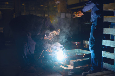 مهندس سعودي داخل مصنع الحديد ، يشرف على العمال و لحام الحديد ، يرتدي العامل قناع حماية  ، شرارة لحام الحديد متناثرة